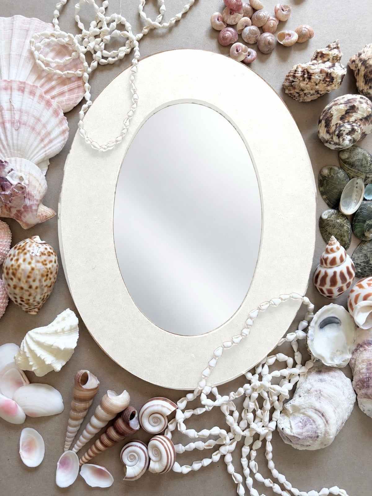 Plain oval mirror frame surrounded by scallops, cowries, spiral shells and shell strands, the supplies for the seashell mirror class